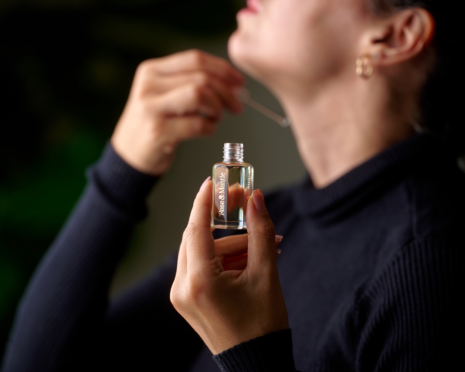 Model applying Rose & Mantle fragrance with the logo visible on the bottle